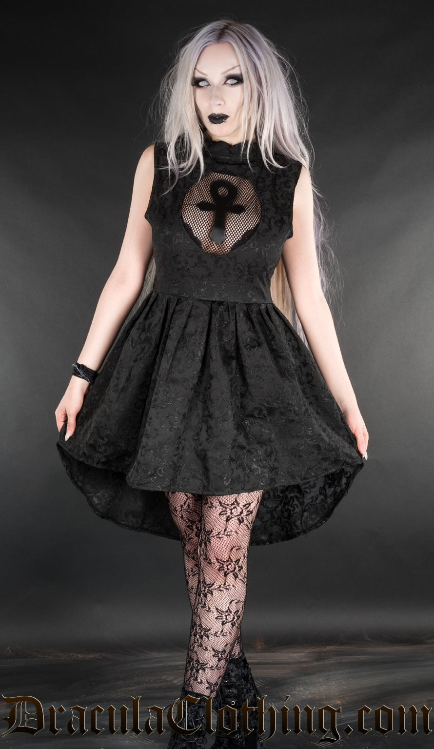 Model wearing short high low style black brocade dress with illusion mesh keyhole cutout featuring ankh motif
