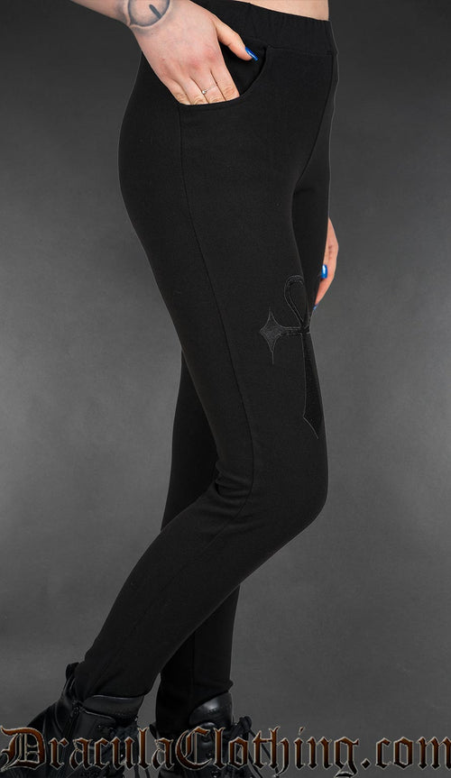 Black gothic high-waisted leggings with embroidered ankh symbols and fitted stretch silhouette worn by a model side view