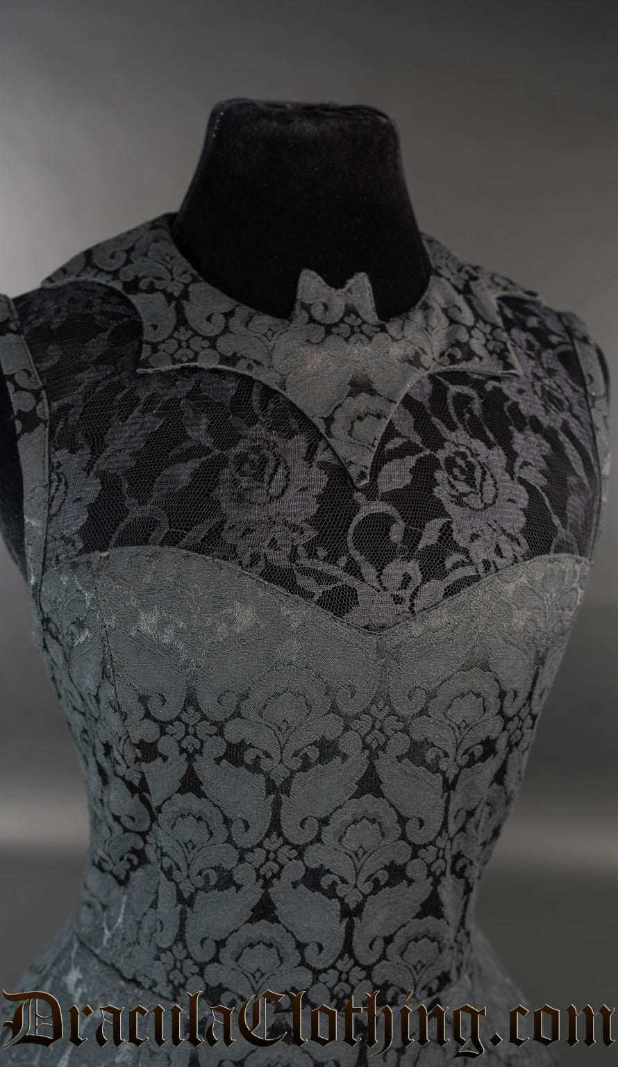 Close up of bat shaped collar and sheer lace illusion chest panel on women's dress made with black cotton brocade fabric in a damask pattern