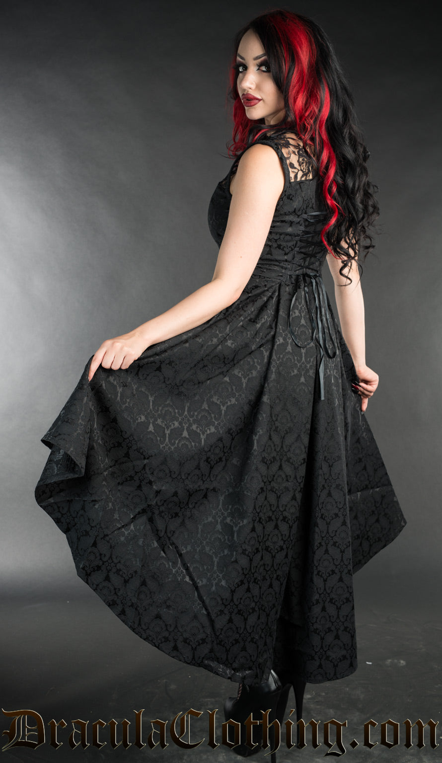 Back view of women's black brocade dress showing longer back of high low style and adjustable corset style lacing in the torso