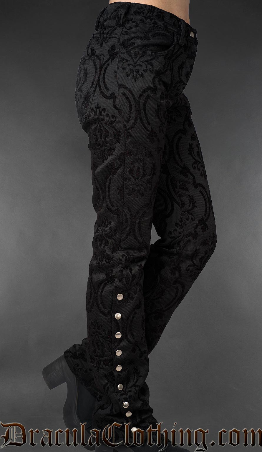 Side view of black gothic brocade officer pants with metal buttons along the lower leg on a gray background