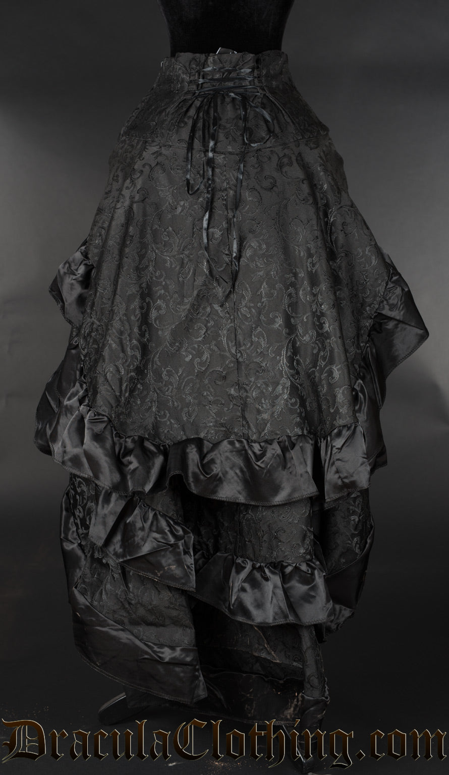 Back view of women's black brocade bustle skirt showing three layers of fabric with black satin hem accents and adjustable lacing in the waist