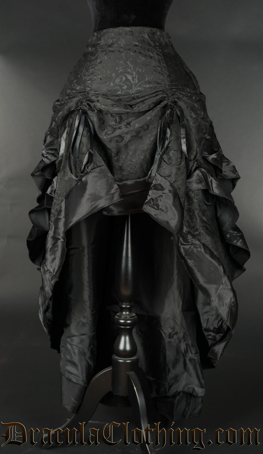 Women's black layered bustle skirt made from brocade fabric and black satin lining shown raised in the front with two strings
