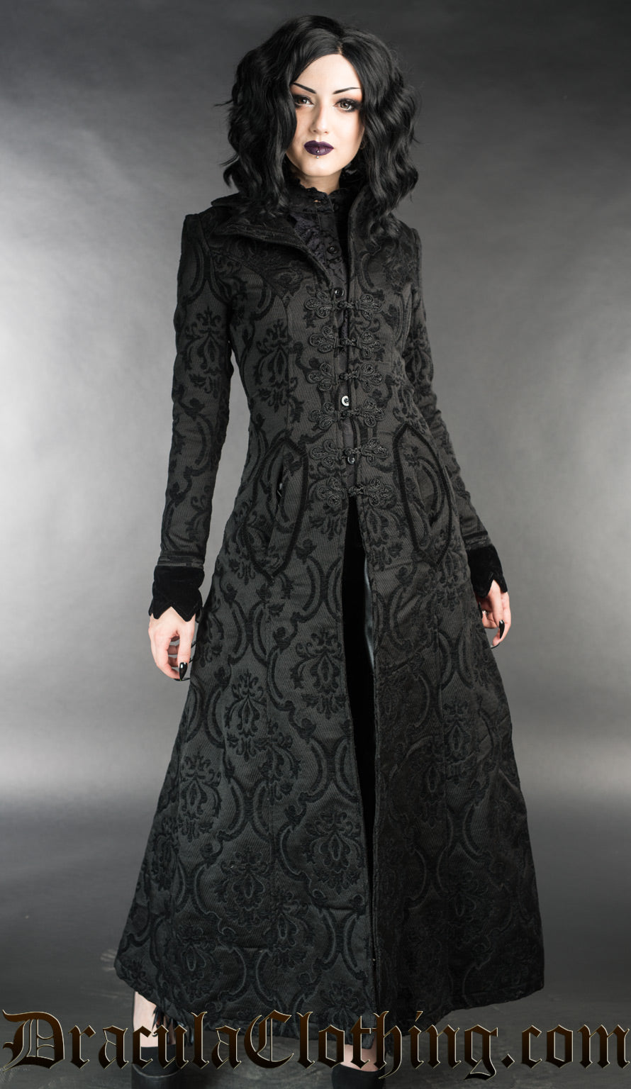 Long women's fitted black coat with knot fastening made from thick black brocade fabric in a damask pattern