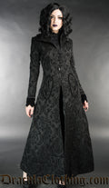 Long women's fitted black coat with knot fastening made from thick black brocade fabric in a damask pattern