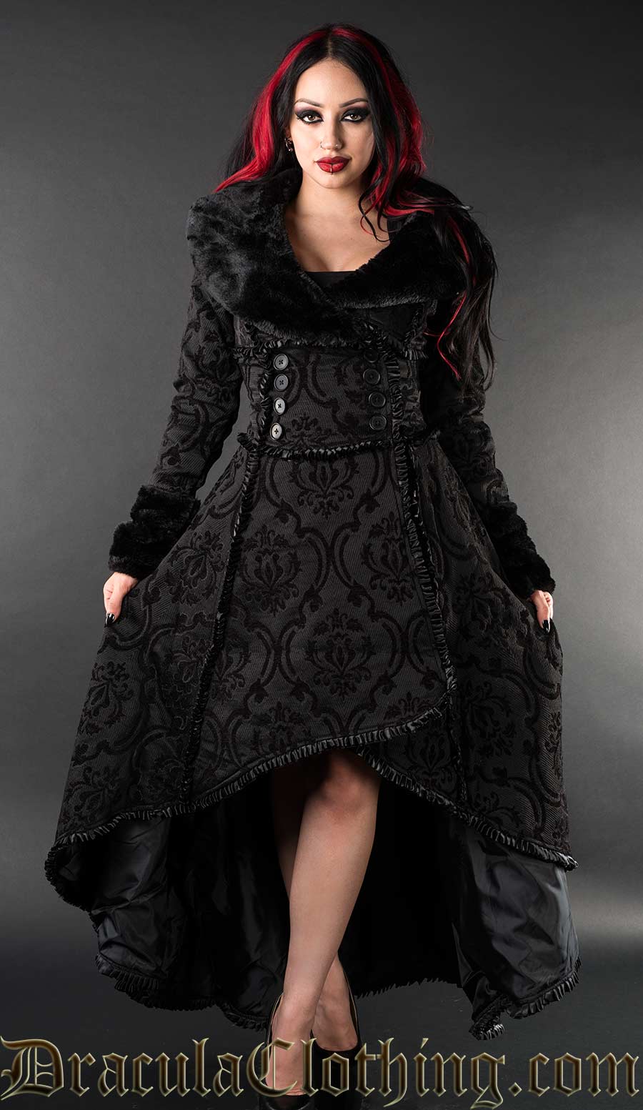 Model wearing women's high low winter coat made with brocade jacquard fabric in a black on black damask pattern and faux fur accents