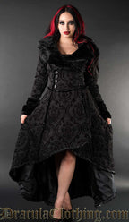 Model wearing women's high low winter coat made with brocade jacquard fabric in a black on black damask pattern and faux fur accents