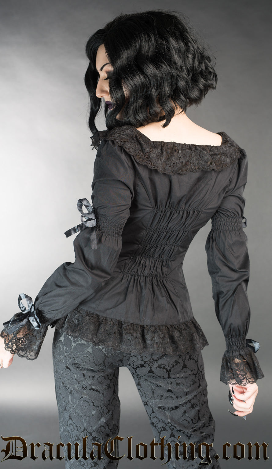 Back view of model wearing women's black long sleeve shirt with elasticated back and lace details