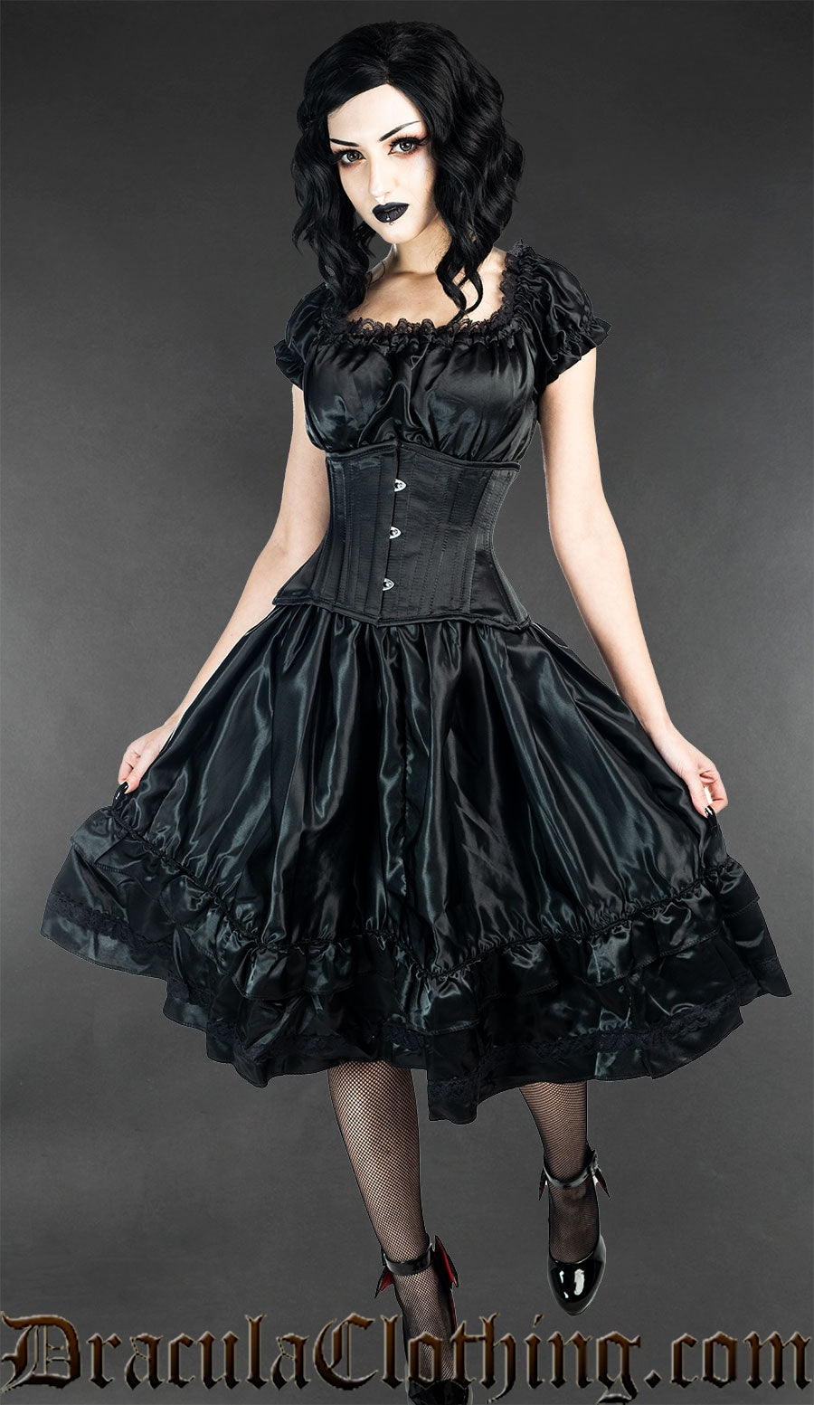 Women's knee length sleeveless black satin dress with lace details worn by a model with additional matching waist cincher