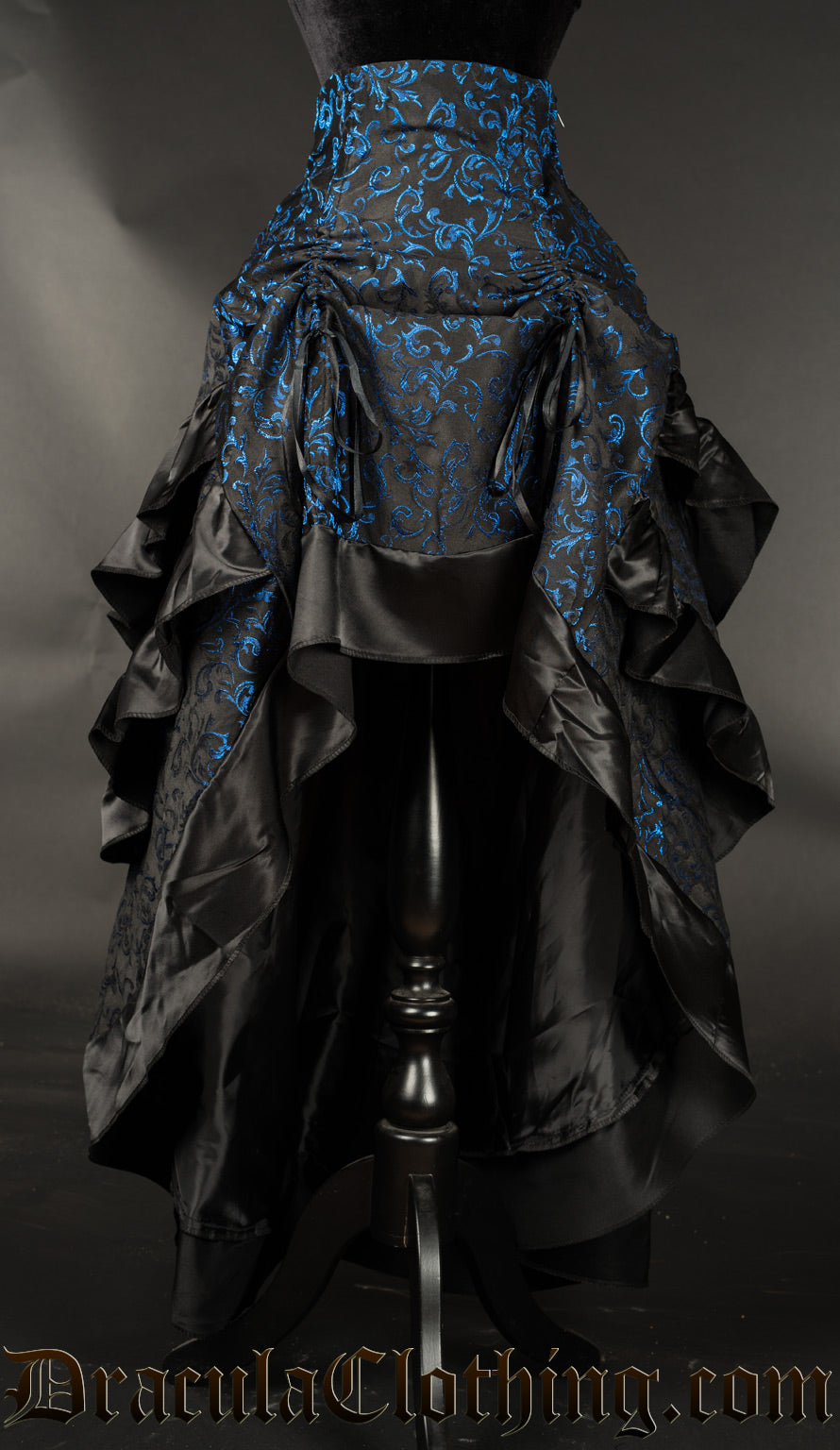Women's layered bustle skirt made from black and blue brocade fabric with black satin hem shown raised in the front