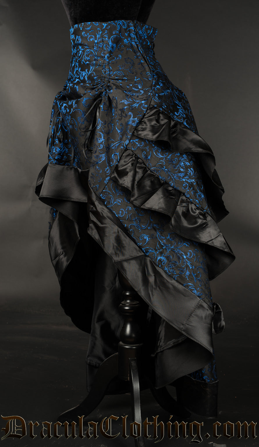 Side view of women's blue brocade bustle skirt showing high low style and three layers in the back for volume