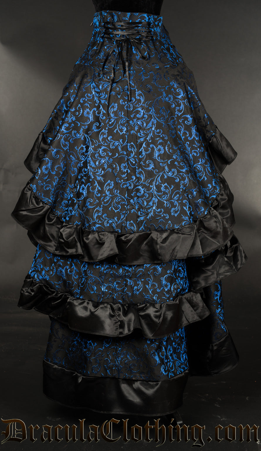 Back view of women's black and blue brocade layered bustle skirt showing adjustable waist lacing and three layers of fabric in the back each with a ruffled black satin hem