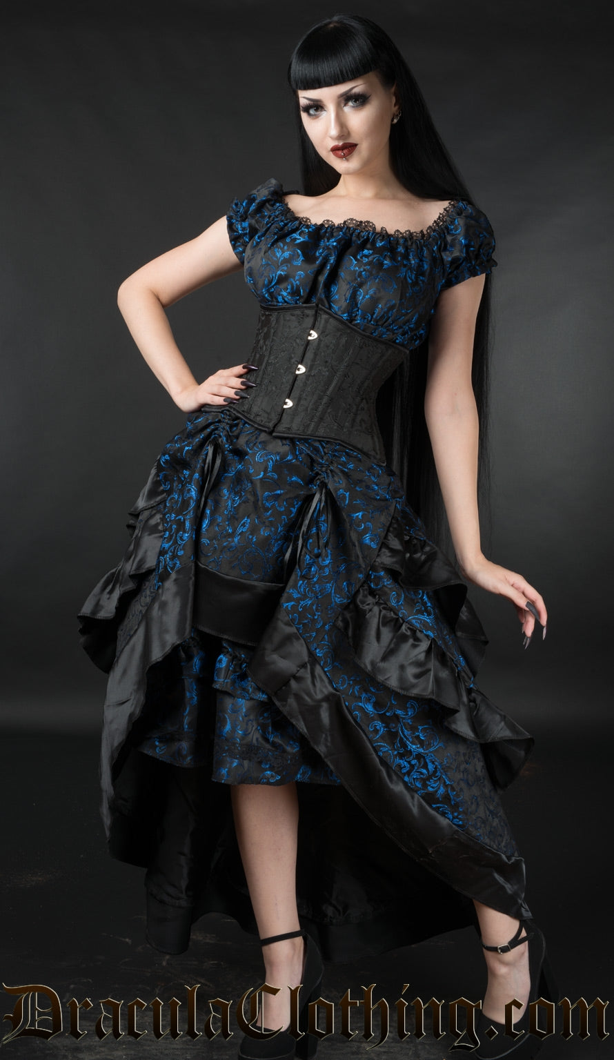 Model wearing black and blue brocade women's bustle skirt over matching gothabilly dress with additional cincher