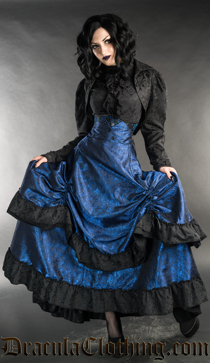 Model wearing blue and black layered bustle skirt with black brocade blouse and bolero jacket