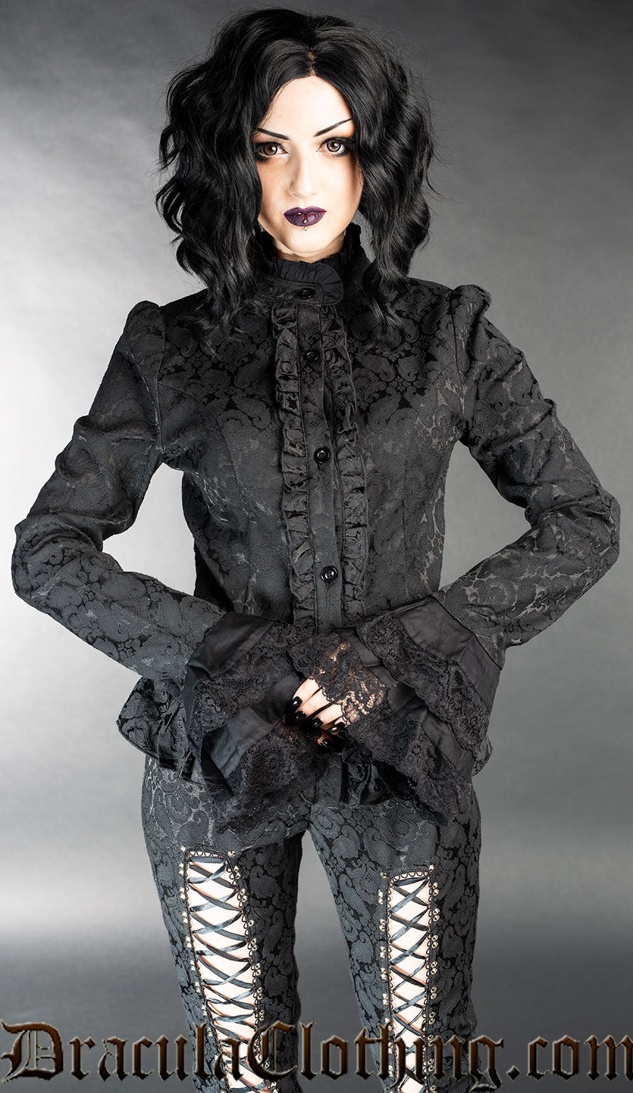 Model wearing long sleeved black brocade women's blouse with flared sleeve cuffs and high neck collar