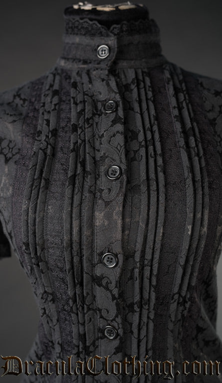 Close up of women's black brocade blouse showing detail of pleated design and lace trim on the high collar