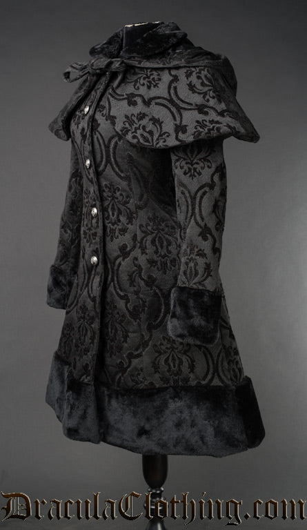 Side view of black jacquard fabric women's coat with damask pattern attached cape and hood and faux fur hem accents