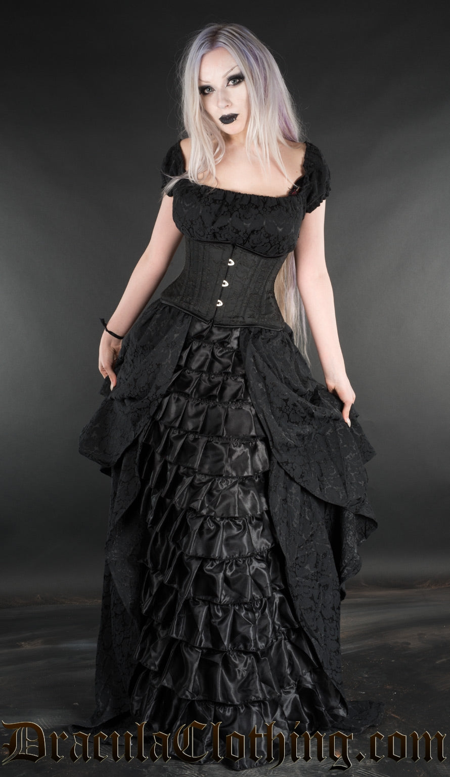 Women's black floor length dress made with brocade fabric and satin ruffles in the centre of the skirt worn by model with additional waist cincher