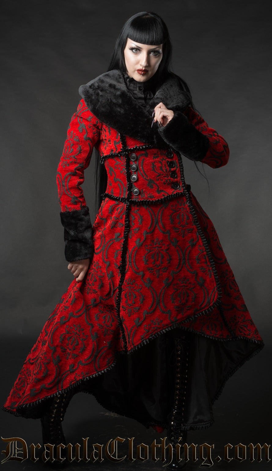 Model wearing red and black high low winter coat made with thick brocade fabric and faux fur accents