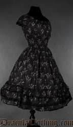 Side view of black knee length women's dress with dragon design showing elasticated sleeves and black lace details on the hem