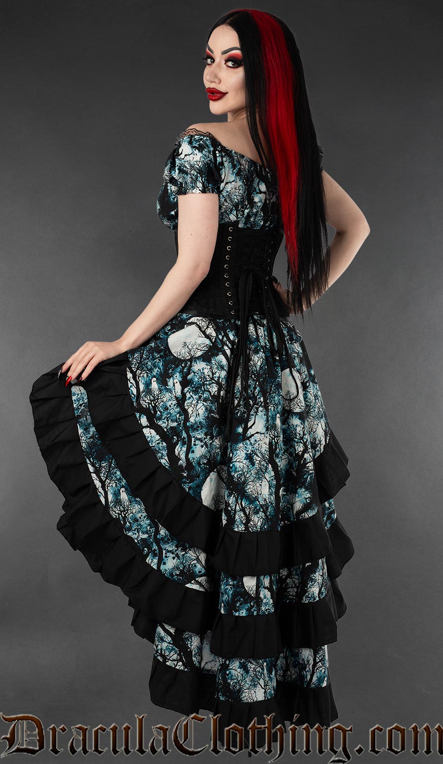 Back view of layered women's bustle skirt featuring a full moon and forest design printed on cotton worn with a matching dress and a waist cincher
