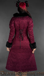 Front view of burgundy gothic brocade coat with black faux fur trim worn by a model on a gray background