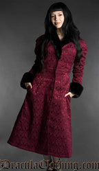 Front view of burgundy gothic brocade coat with black faux fur trim worn by a model on a gray background