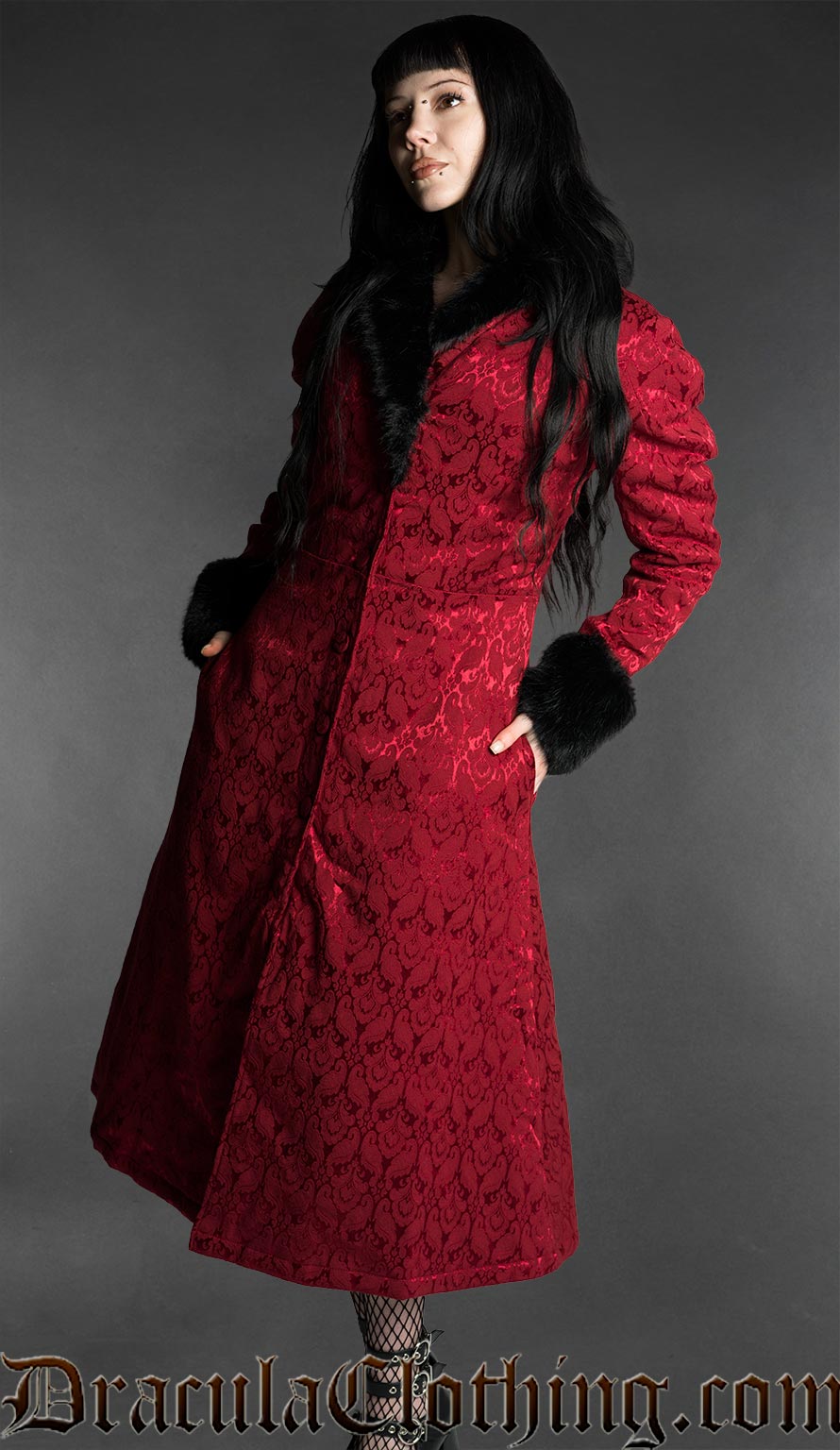 Red gothic brocade coat with black faux fur trim worn by a woman on a gray background