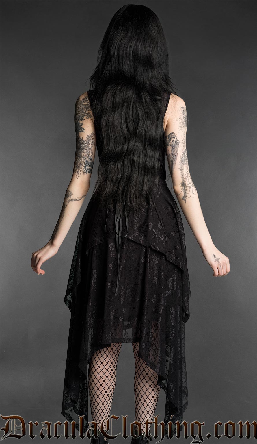 Woman wearing a black gothic mourning dress with lace material, fitted bodice and flowing layered handkerchief hem back view