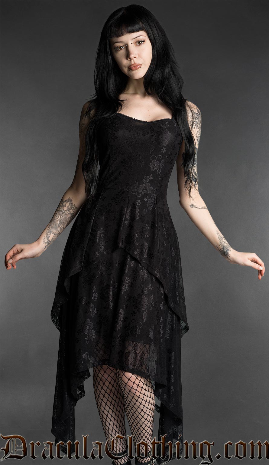 Woman wearing a black gothic mourning dress with lace material, fitted bodice and flowing layered handkerchief hem