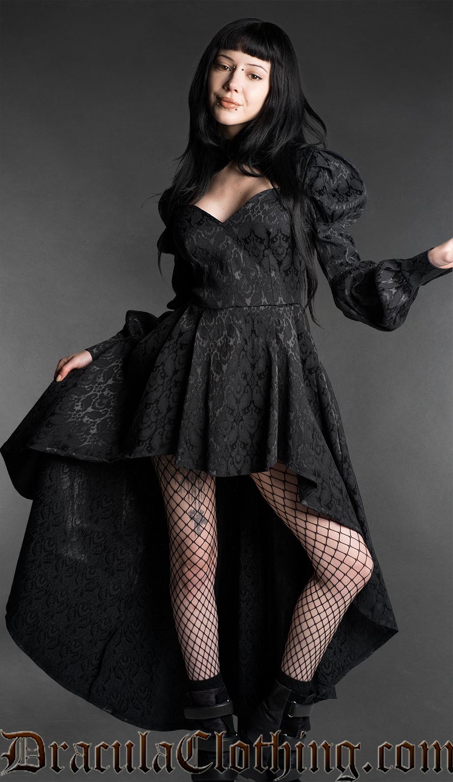 Woman wearing a black neo-Victorian high-low dress with floral brocade fabric, sweetheart neckline and puff bishop sleeves