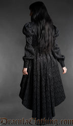 Woman wearing a black neo-Victorian high-low dress with floral brocade fabric, sweetheart neckline and puff bishop sleeves back view