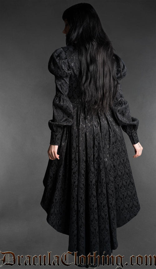 Woman wearing a black neo-Victorian high-low dress with floral brocade fabric, sweetheart neckline and puff bishop sleeves back view