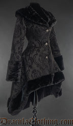 Side view of women's black coat made with thick brocade fabric and faux fur showing shorter high low style hem