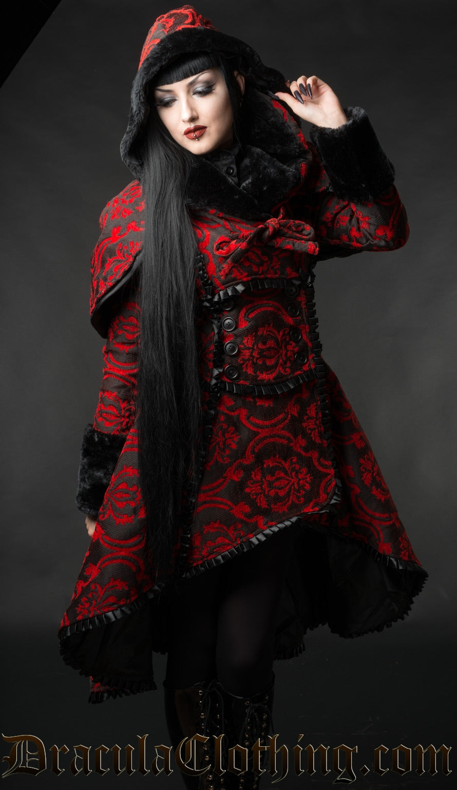 Model wearing red and black brocade winter coat with additional matching hood and cape