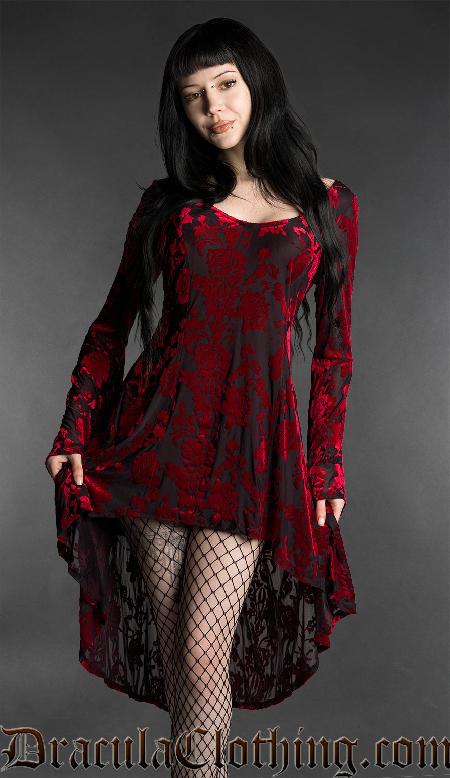 Woman wearing a black and red gothic burnout velvet high-low dress with rose pattern, long flared bell sleeves, square neckline and flowing asymmetrical hem
