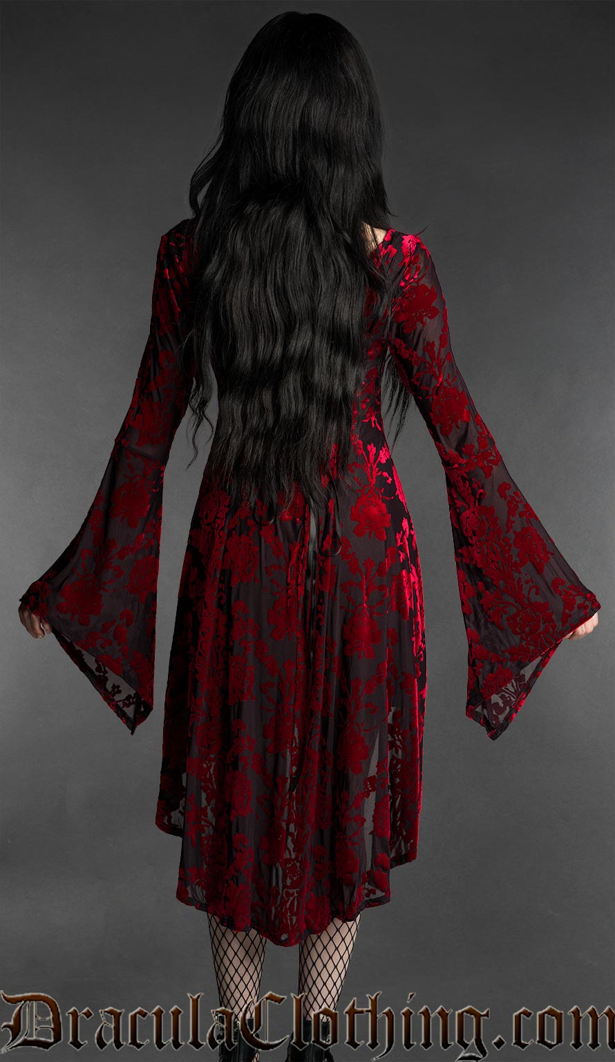 Woman wearing a black and red gothic burnout velvet high-low dress with rose pattern, long flared bell sleeves, square neckline and flowing asymmetrical hem back view
