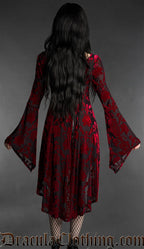 Woman wearing a black and red gothic burnout velvet high-low dress with rose pattern, long flared bell sleeves, square neckline and flowing asymmetrical hem back view