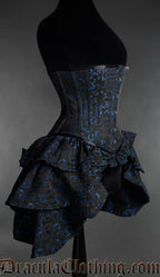 Side view of black and blue woven brocade corset showing layered ruffled bustle fabric