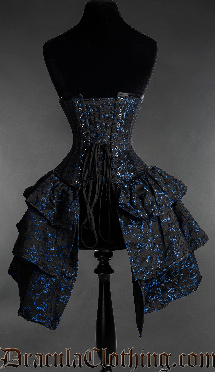Back view of black and blue woven brocade corset with bustle skirt attachment showing adjustable lacing and matching fabric modesty panel