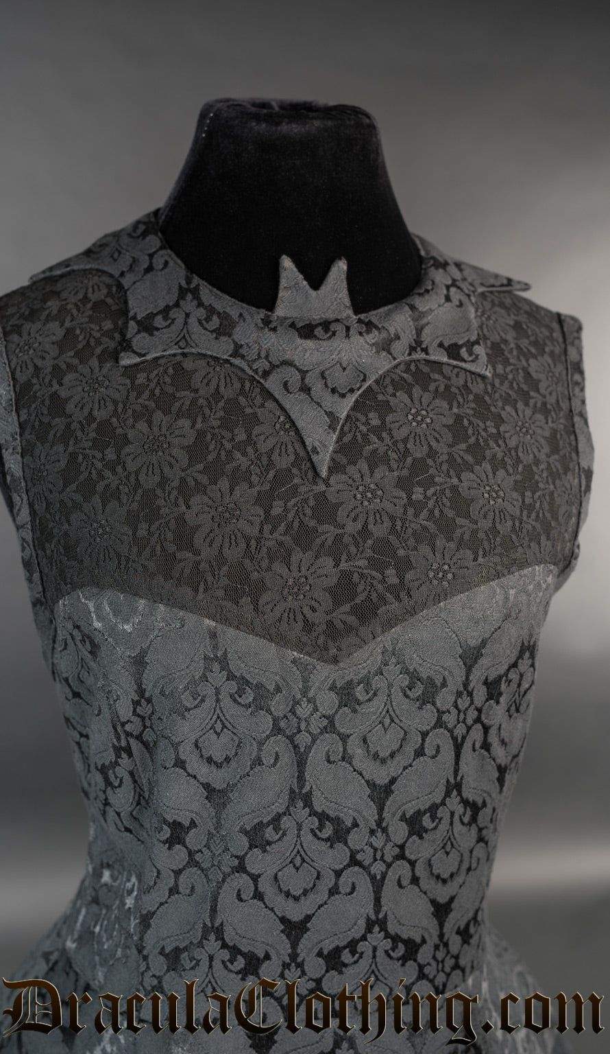 Close up of women's black brocade dress showing bat shaped collar and sheer lace chest panel