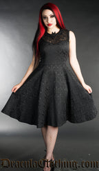 Model wearing knee length black brocade dress with lace chest and bat shaped collar