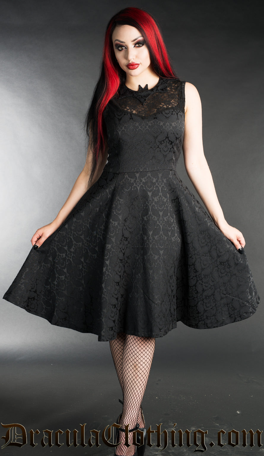 Model wearing knee length black brocade dress with lace chest and bat shaped collar