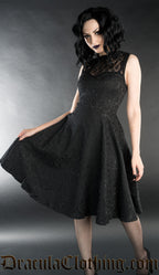 Model wearing knee length black brocade dress with bat collar and lace