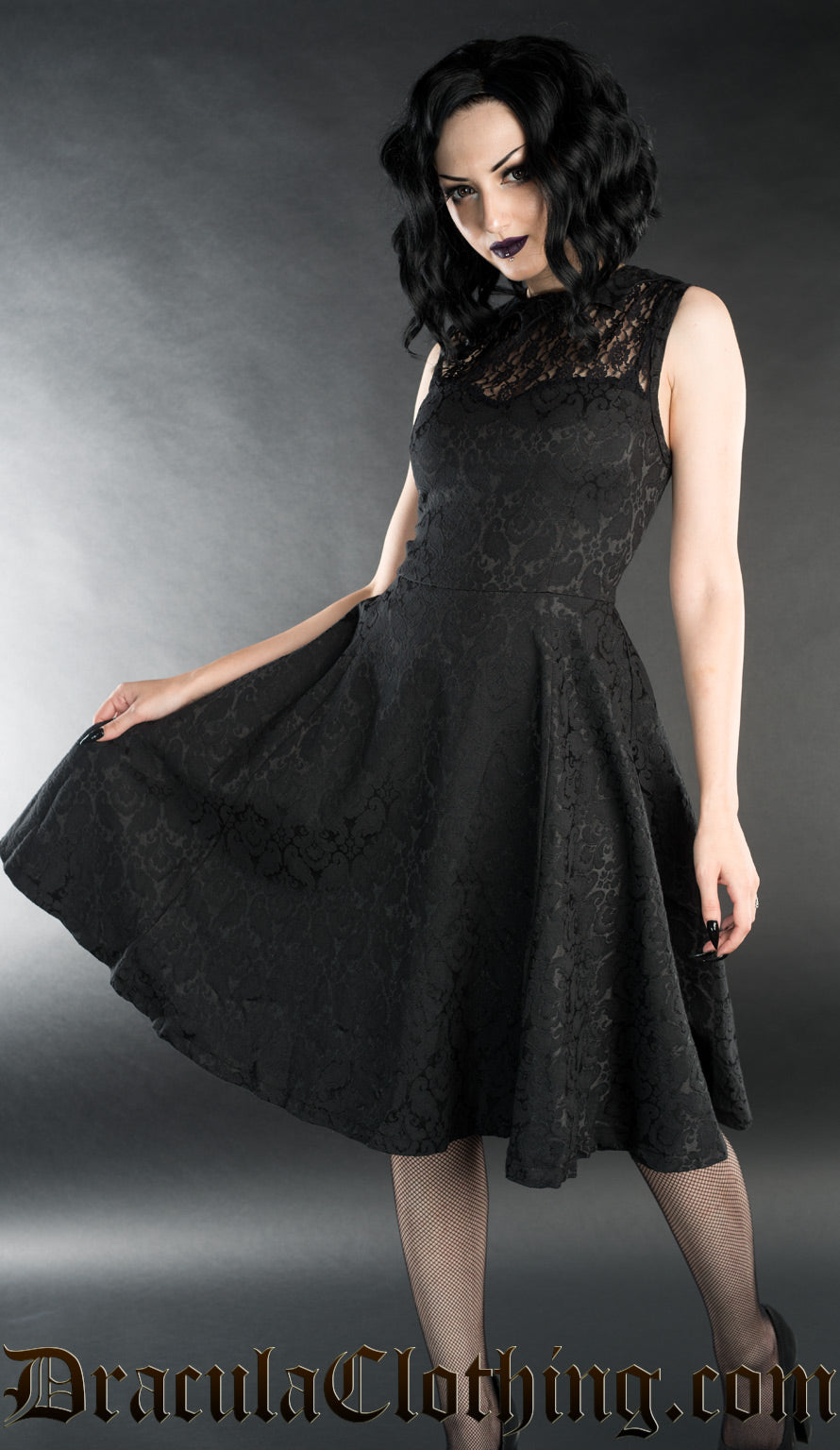 Model wearing knee length black brocade dress with bat collar and lace