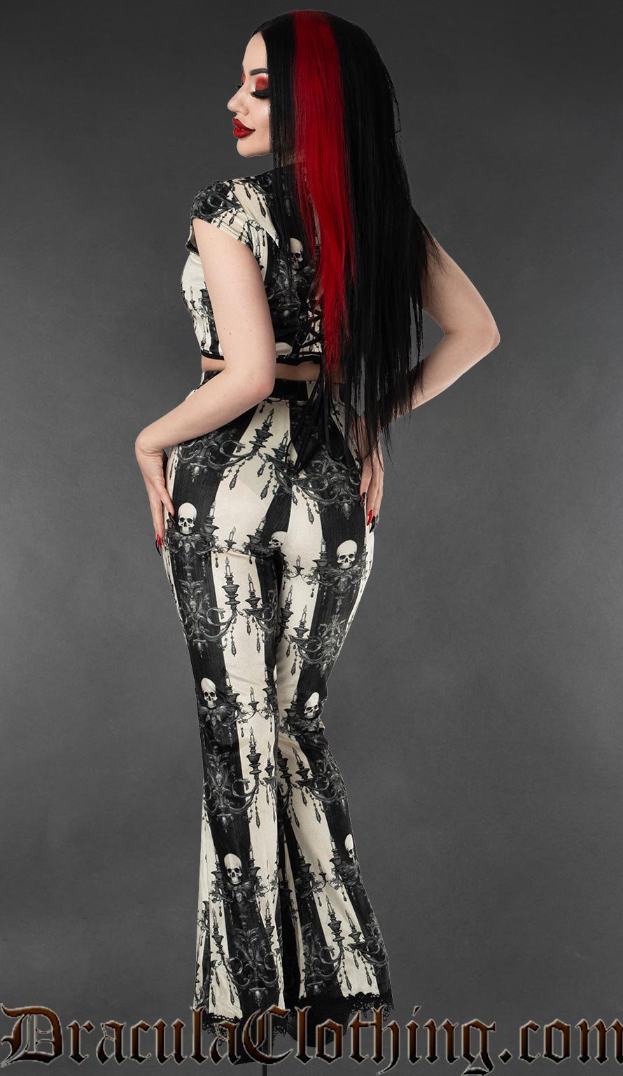 Model wearing black and white skull striped velvet flare pants with matching gothic crop top back view