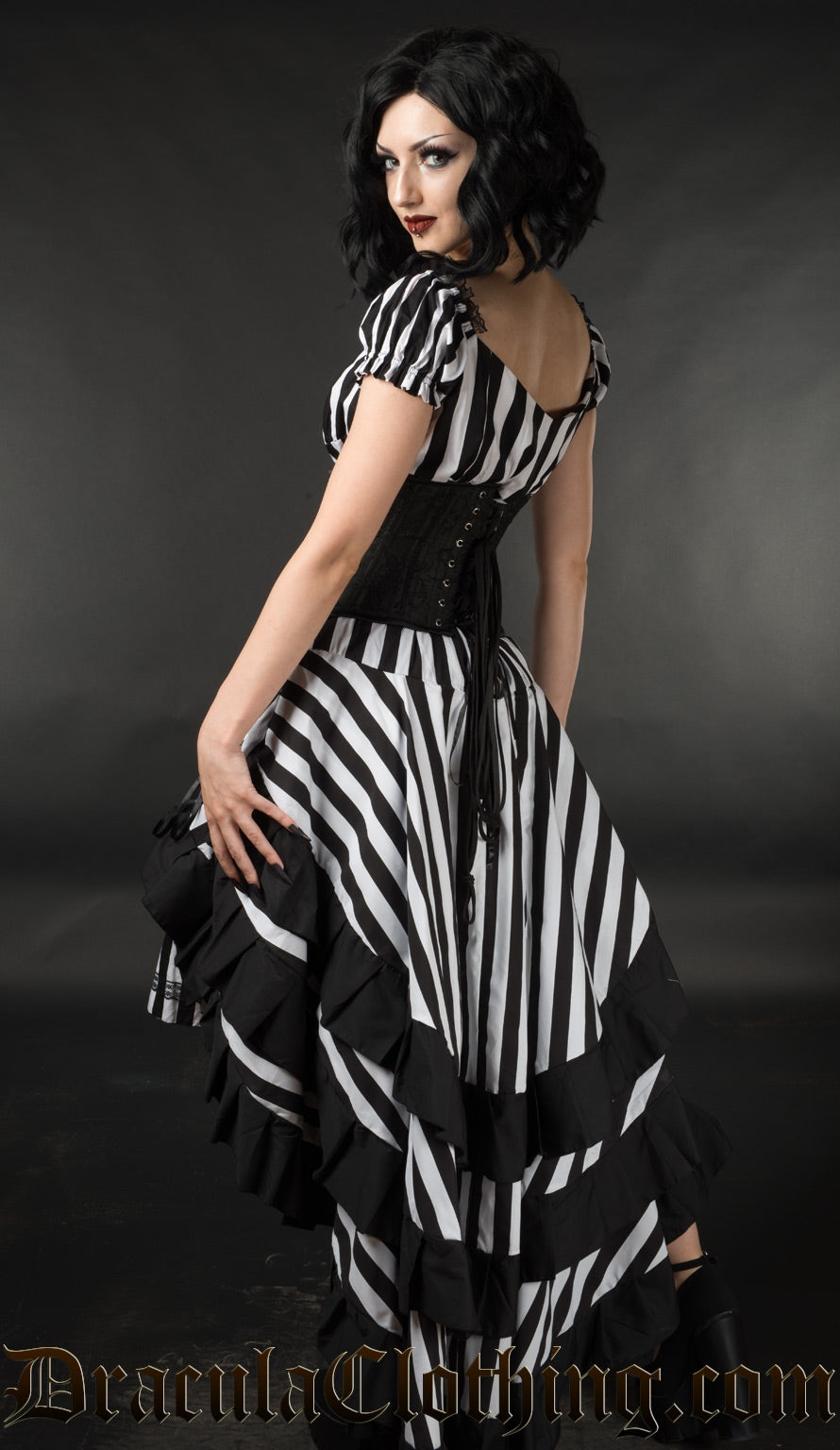 Back view of black and white striped women's layered bustle skirt with black hem trim worn with a waist cincher and matching striped dress