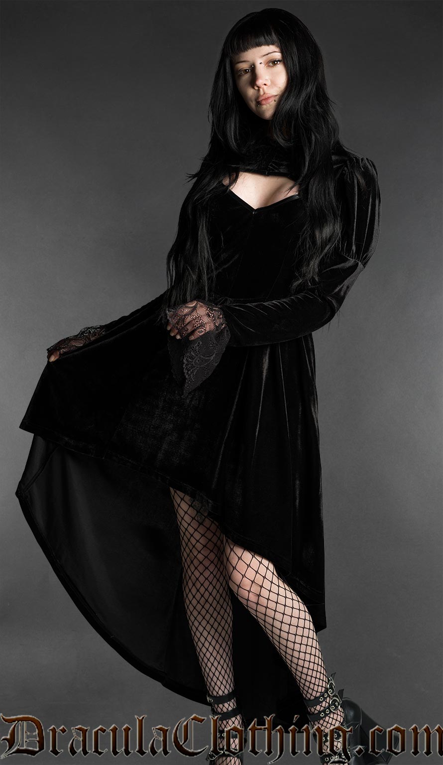 Woman wearing a black gothic velvet vampire dress with sweetheart neckline, lace bell sleeves and high-low hem