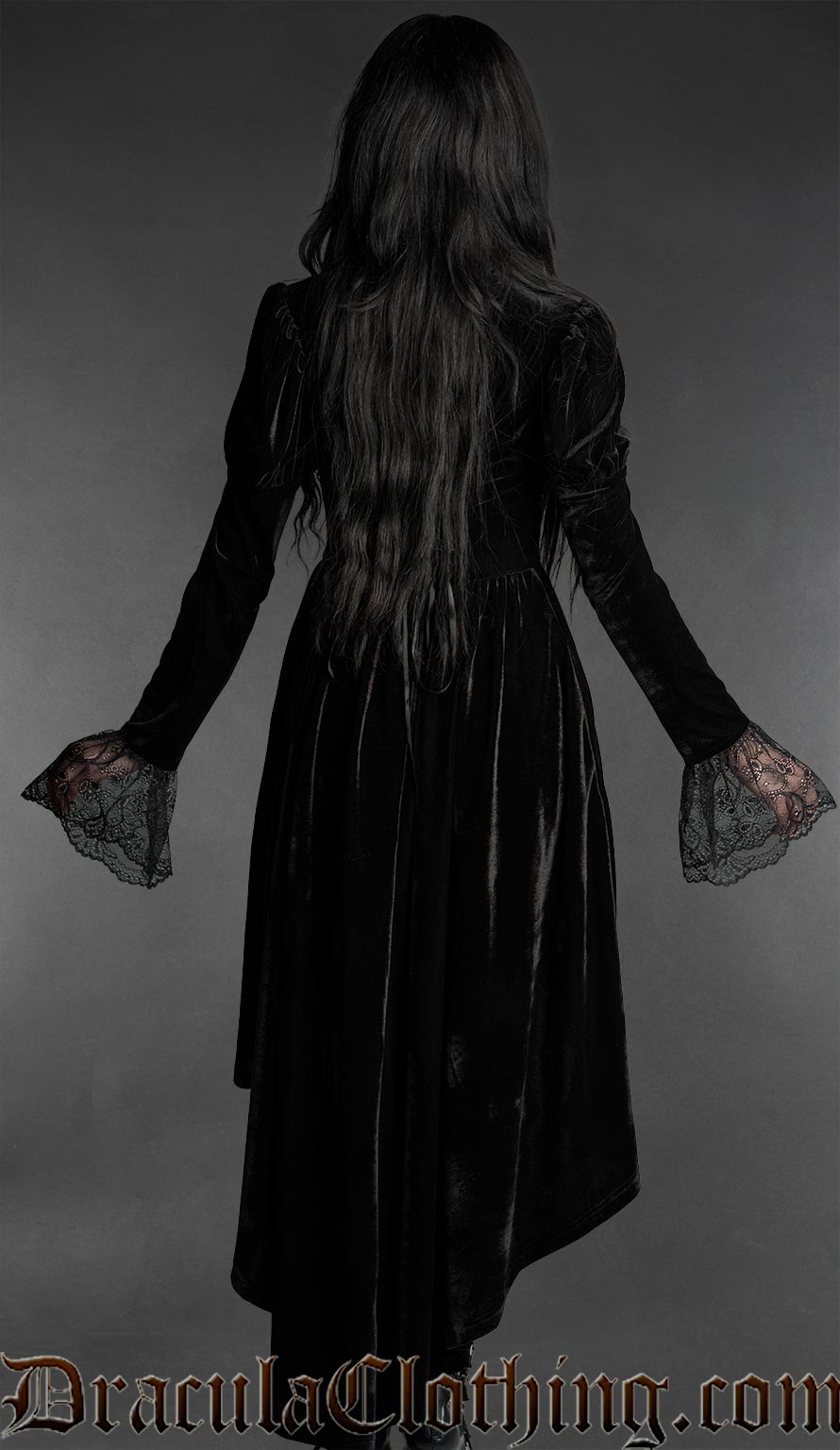 Woman wearing a black gothic velvet vampire dress with sweetheart neckline, lace bell sleeves and high-low hem back view